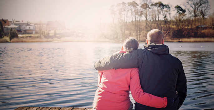 Retro filtered photo of a couple sitting on wooden pier by lake.