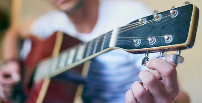 Close-up of young caucasian man tuning a guitar