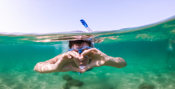 head-on underwater photo of caucasian male snorkeling and making heart shape with hands
