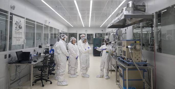 five adults in white hazmat suits touring cleanroom facility