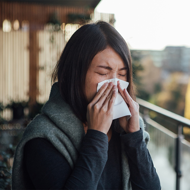 Woman using tissue on nose on balcony