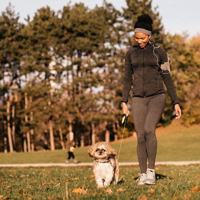 Woman walks in a field with a small dog on a leash