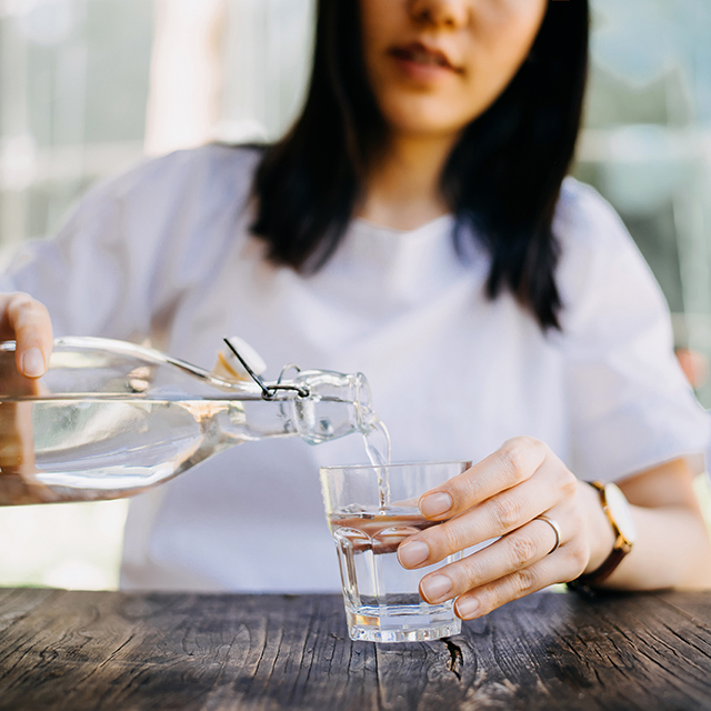 A woman pours water from a large bottle into a small drinking cup at an outdoor table.