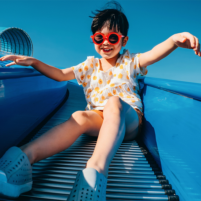 Asian child in sunglasses on slide with feet in foreground