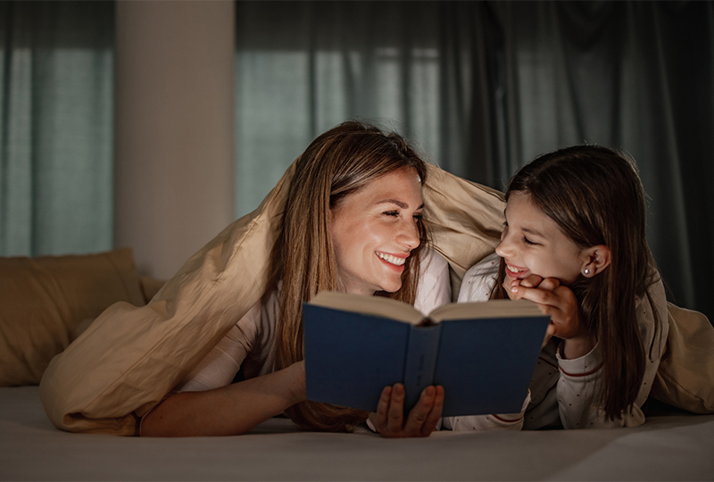 Mom and daughter reading book in bed