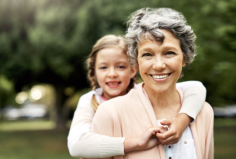 An older woman gets a hug from a girl standing behind her.