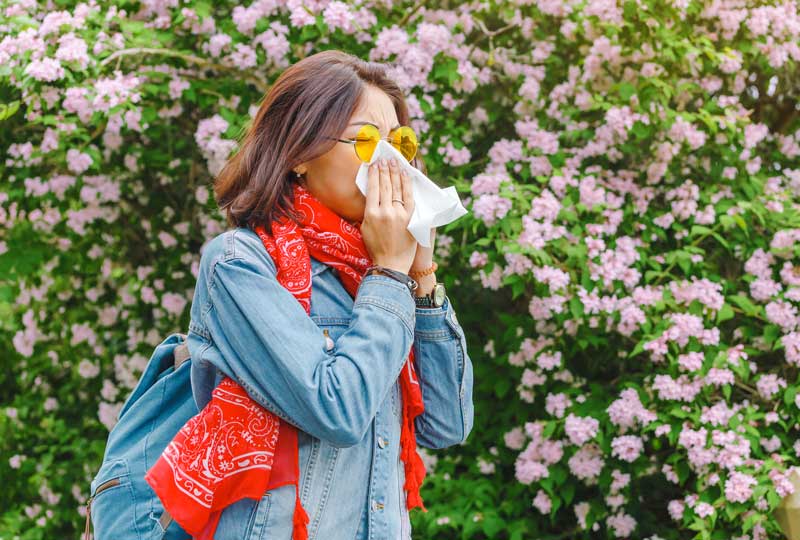 Woman experiencing symptoms of allergies, blowing nose in tissue