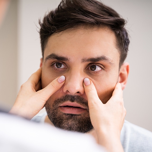 Man having his sinuses checked. Woman's hands pressing on face on either side of nose.