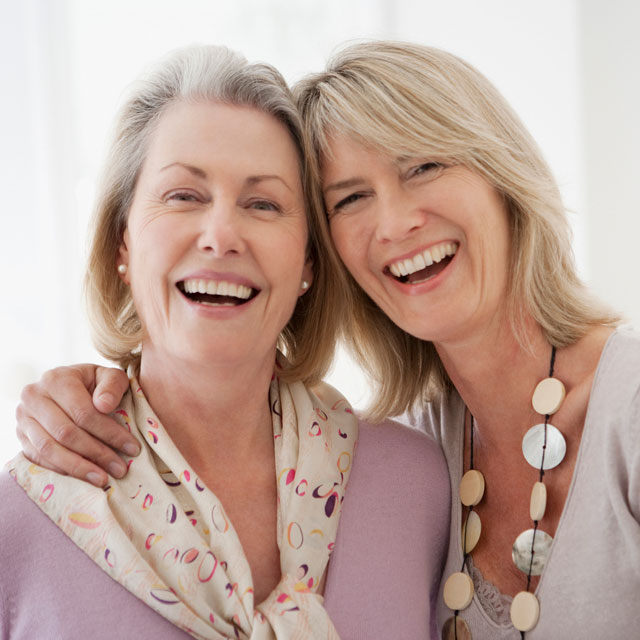 Two middle aged sisters embrace looking into the camera