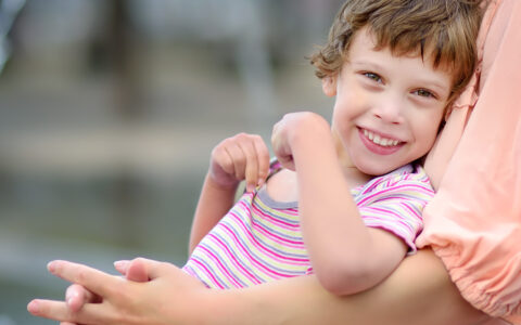 Close-up portrait of beautiful smiling disabled child in the arms of mother.