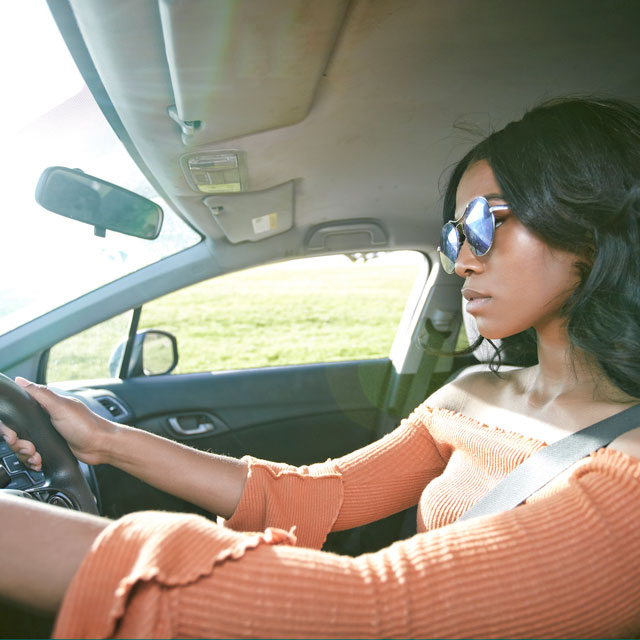 Young woman drives a car along a grassy field