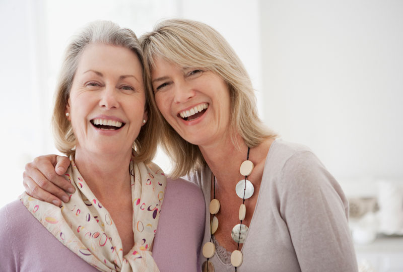 Two middle aged sisters embrace looking into the camera