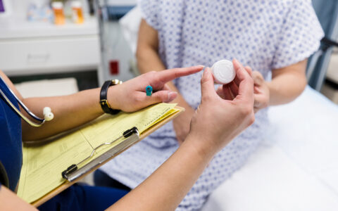 A nurse holding a clipboard explains the label of a prescription bottle to a patient.