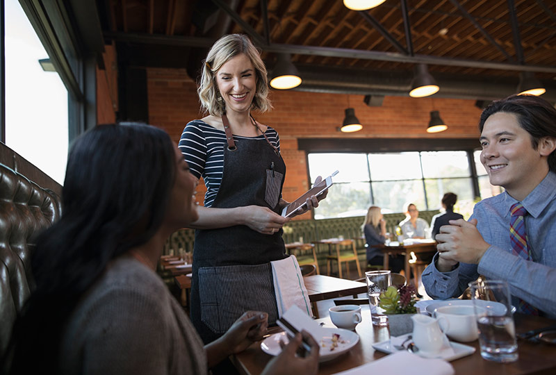 Two people at a restaurant table talk with the server.