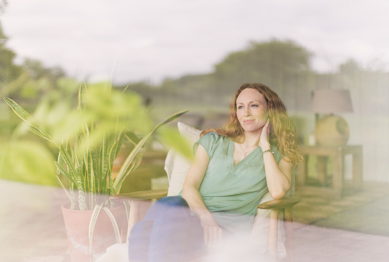 Woman sits in armchair looking wistfully through a window