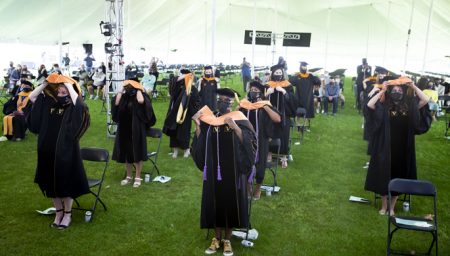 Graduates stand and don their academic hoods in a ceremonial group hooding.