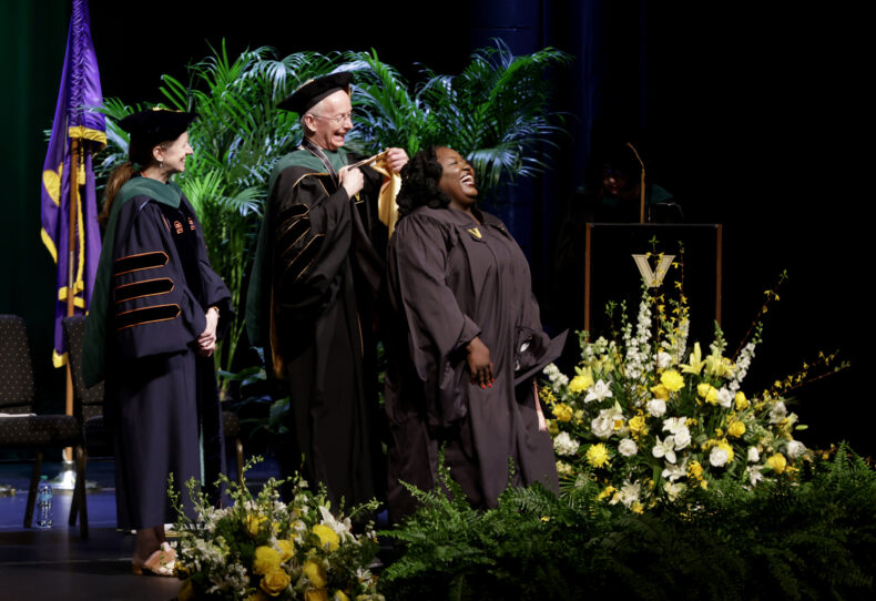 The face of Benmun Damul, MPH, tells the story of her joy as she receives her hood as a Master of Public Health graduate from Don Brady, MD, as Amy Fleming, MD, MScHPE, looks on. (photo by Donn Jones)