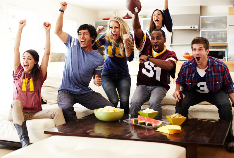 Group of friends in a living room getting excited about a football game on TV