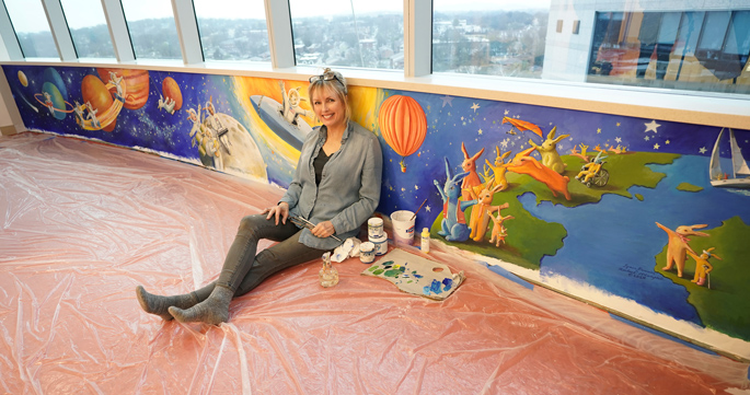 Artist Rachael McCampbell poses with her mural, “Space Bunnies,” on the 11th floor or Monroe Carell Jr. Children’s Hospital at Vanderbilt.