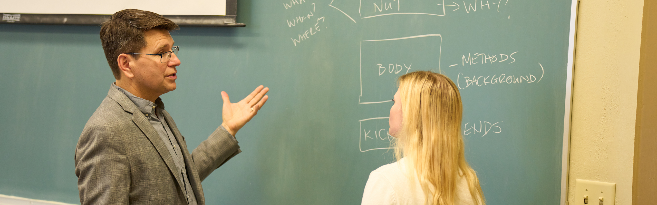 Professor in conversation with student by chalkboard