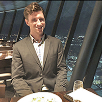Devon Akers sitting at a table in a restaurant with a window and night view of a city in the background