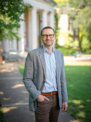 Christoph Zeller standing outside in front of a collonaded building with trees and grass in the background