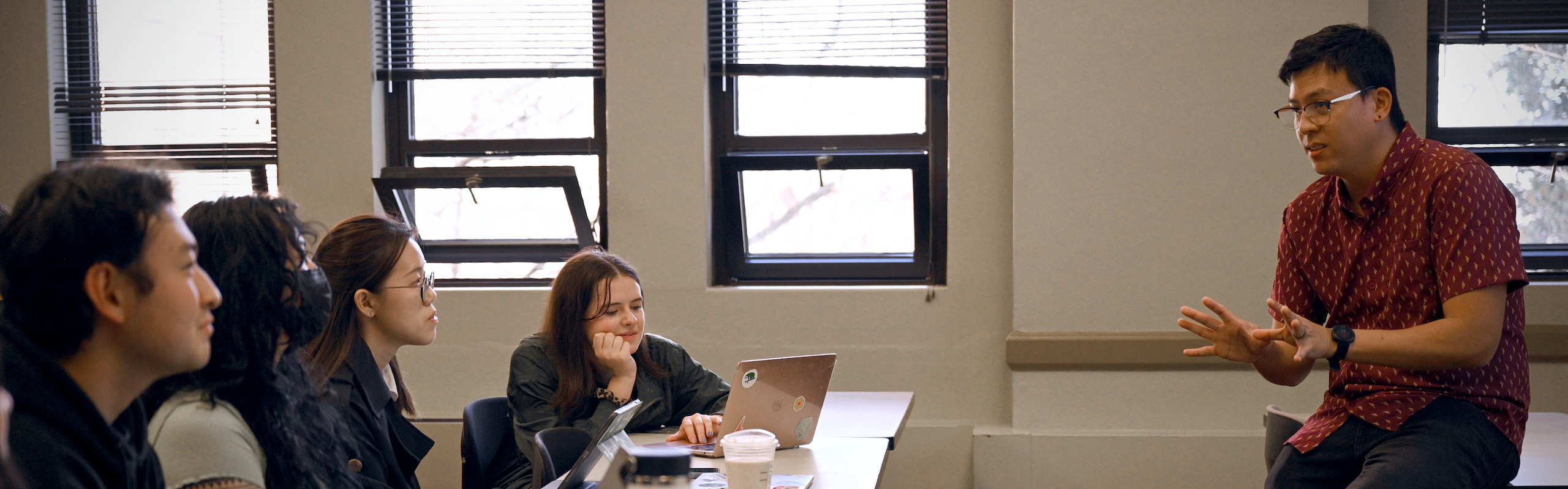 Professor sitting on desk speaking with students in class