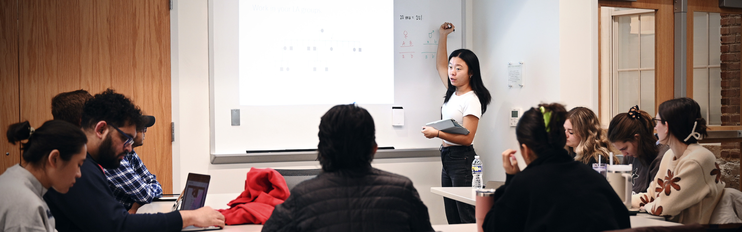 Student writing on white board while addressing the class