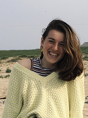 Natalie Elliott sitting on a beach with grass and sand in the background