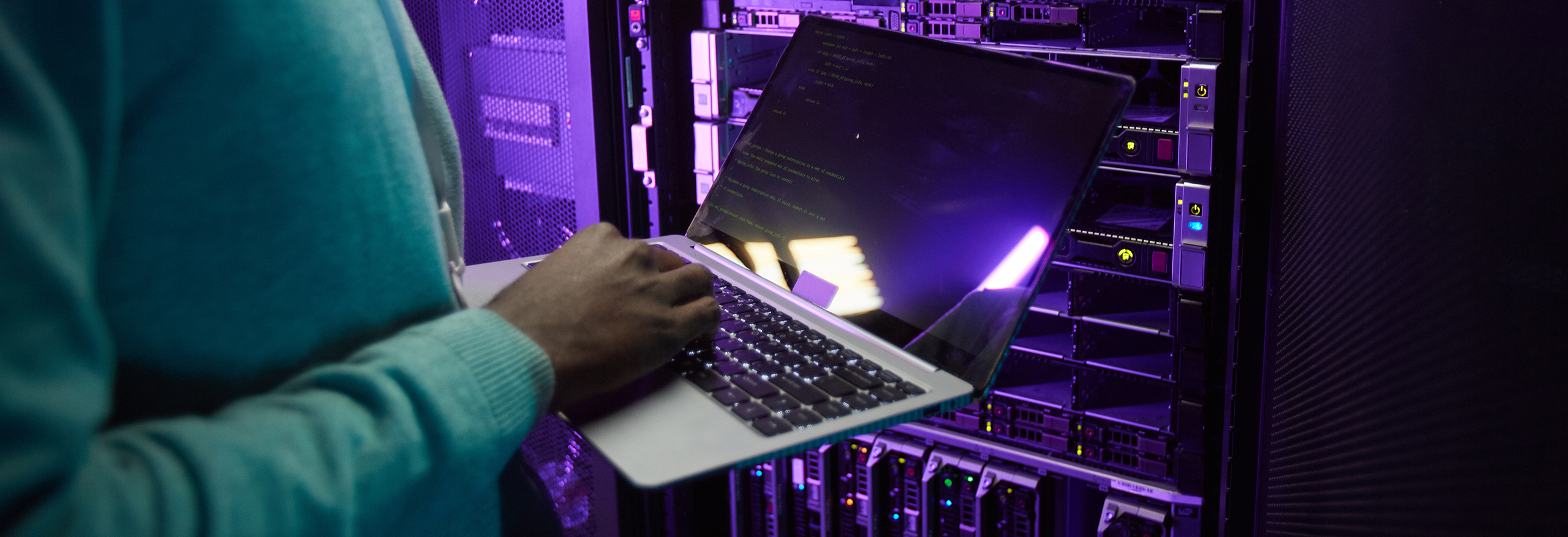 Cropped shot of African American data engineer holding laptop while working with supercomputer in server room lit by blue light, copy space