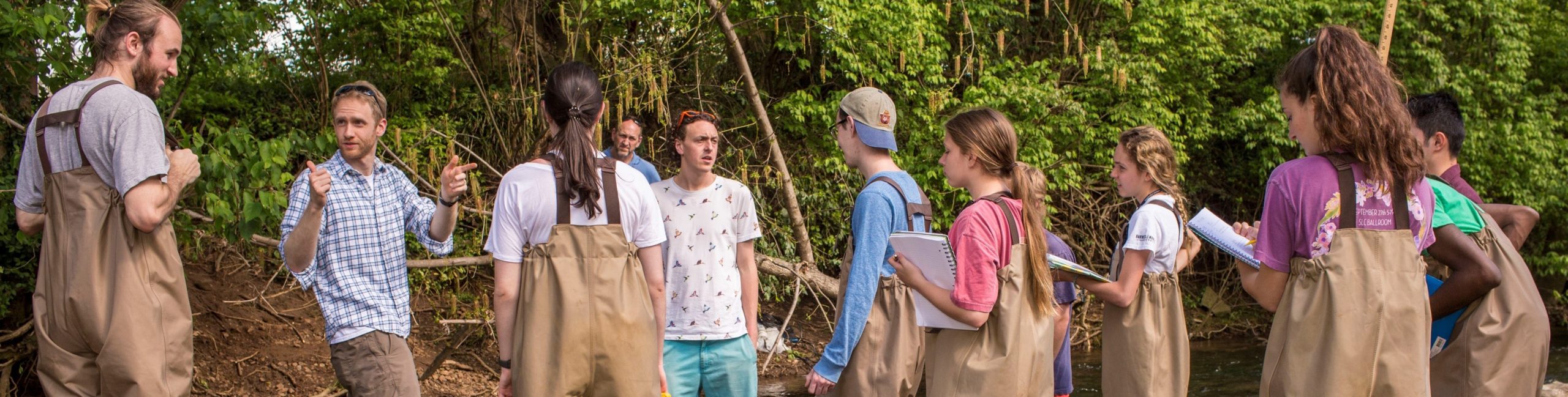 Dr. Tate directs students who hold notebooks while wearing gear to work in water