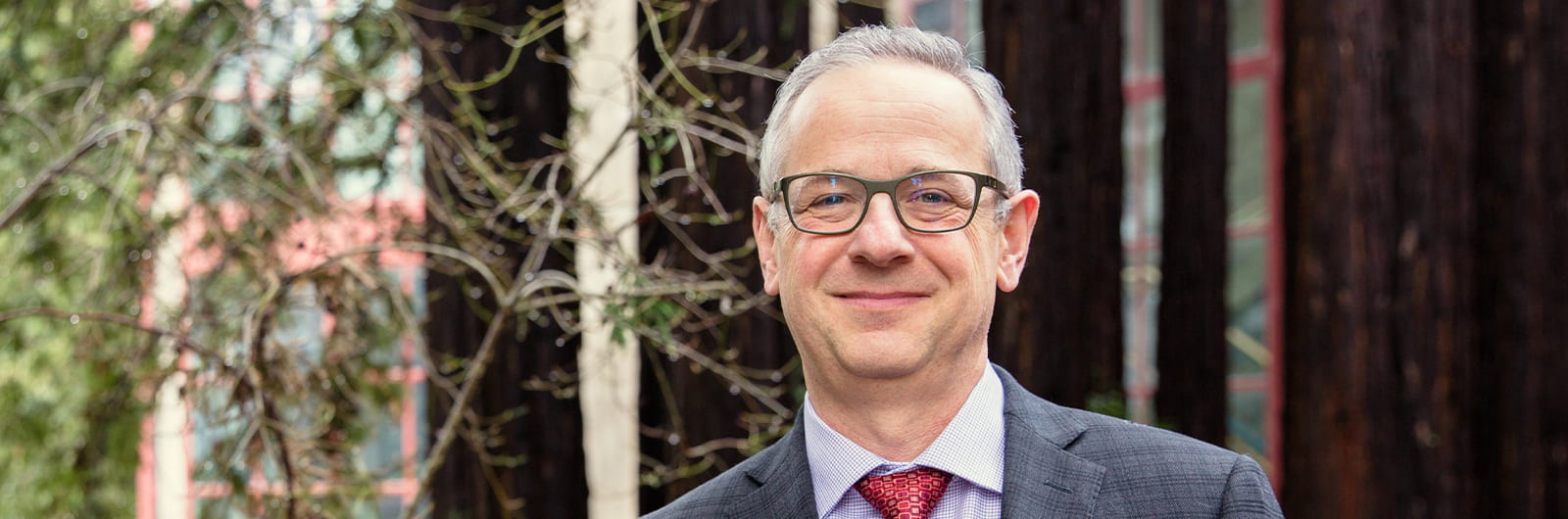 Paul Koch in grey suit, blue shirt, red tie, smiling