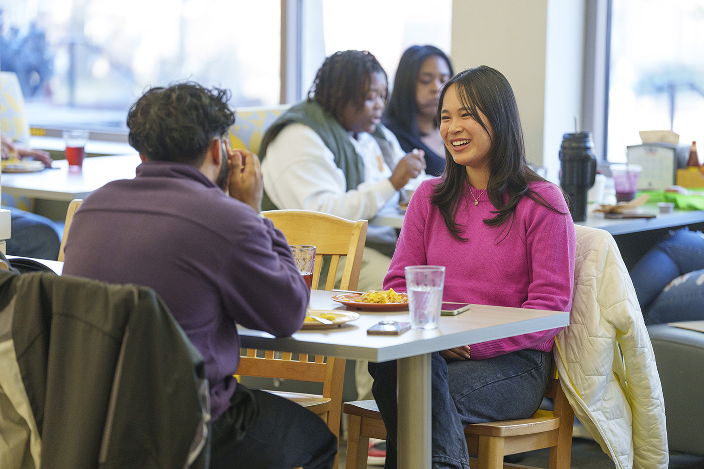 two students sit across from each other at a dining hall while smiling