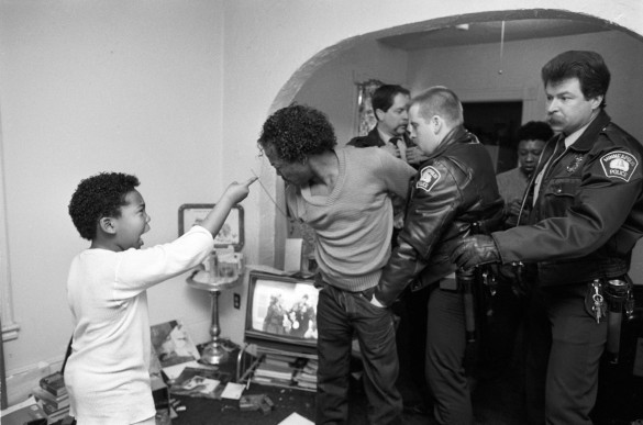 Boy pointing at shirtless man being arrested in home