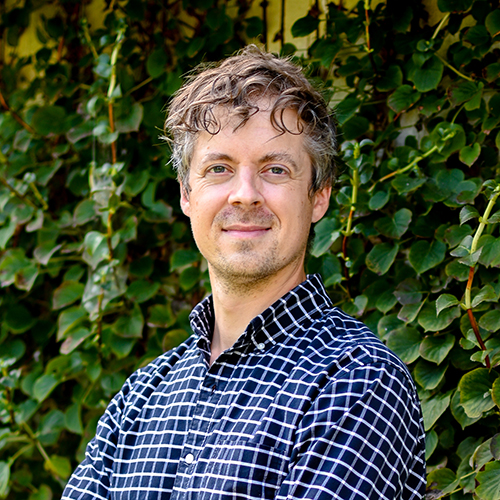 James Moore standing in front of green foliage.