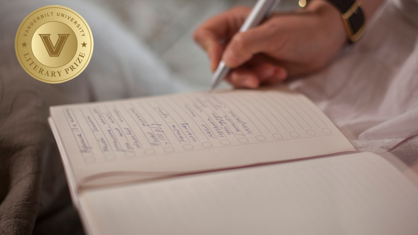 A hand holding a pen writes in a notebook. In the corner of the image is the logo for the Vanderbilt University Literary Prize.