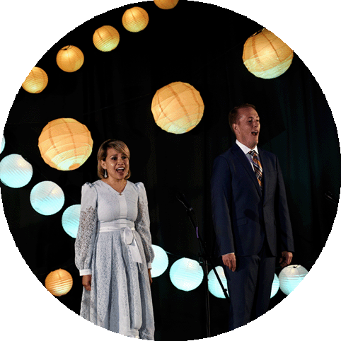 Two opera singers perform with bright paper lanterns in background