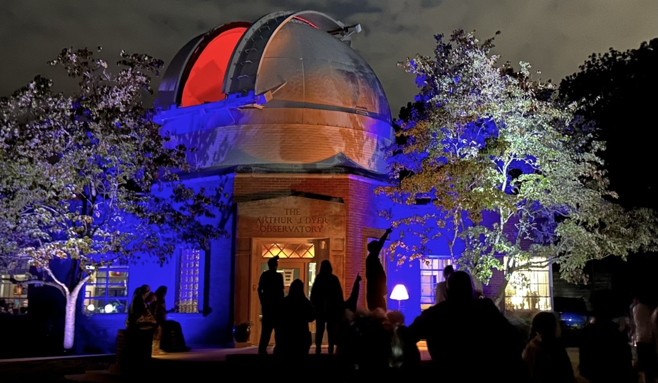 Silhouettes of people pointing to the sky in front of Dyer Observatory at night