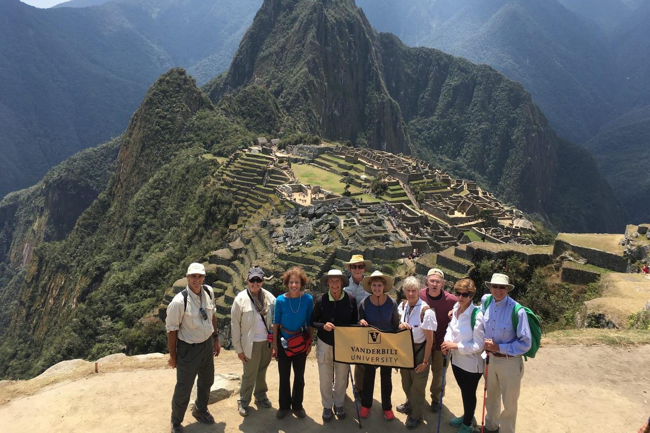 A group of people holding a Vanderbilt flag standing in front of the ancient Incan ruins of Machu Picchu, a famous archaeological site in Peru.