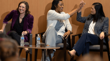 Pictured: Panelists at Vanderbilt Business’ Executive Women in Leadership: New Leadership Strategies for 2024 event. The 3 panelists are sitting on a stage. Allie Feiner is on the left, Candice Storey Lee is in the middle, and Jennifer Hutcheson is on the right. Feiner is laughing, Lee and Hutcheson are giving each other a high five.