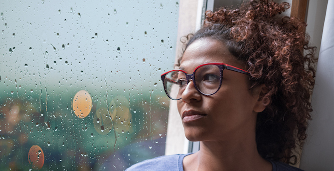 Sad african american woman looking out of the window on rainy weather