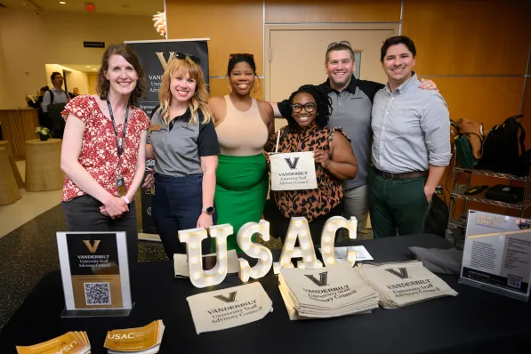 A group of men and women standing behind a booth with lit signage reading "USAC"