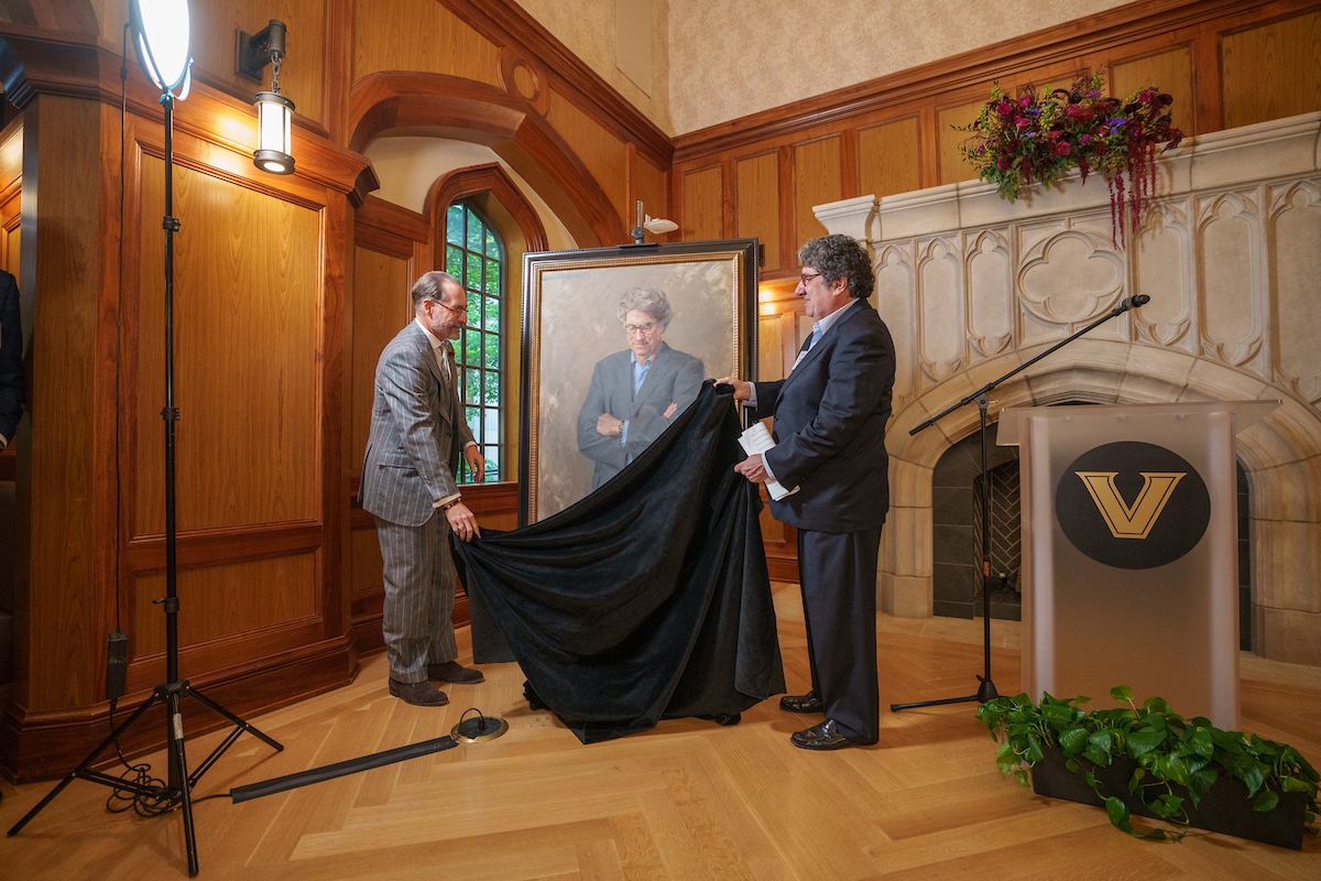 Two men pulling a black sheet off of a portrait