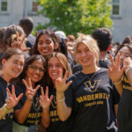 Four first-year students wearing matching black Vanderbilt shirts show the VU hand sign at Move-in