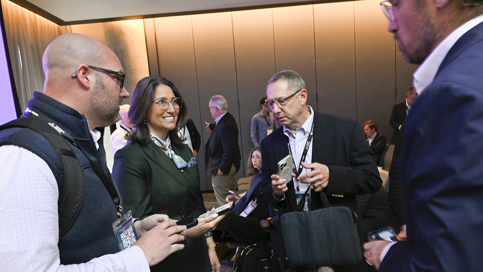 A group of men and women in business attire standing around talking with smart phones in hand