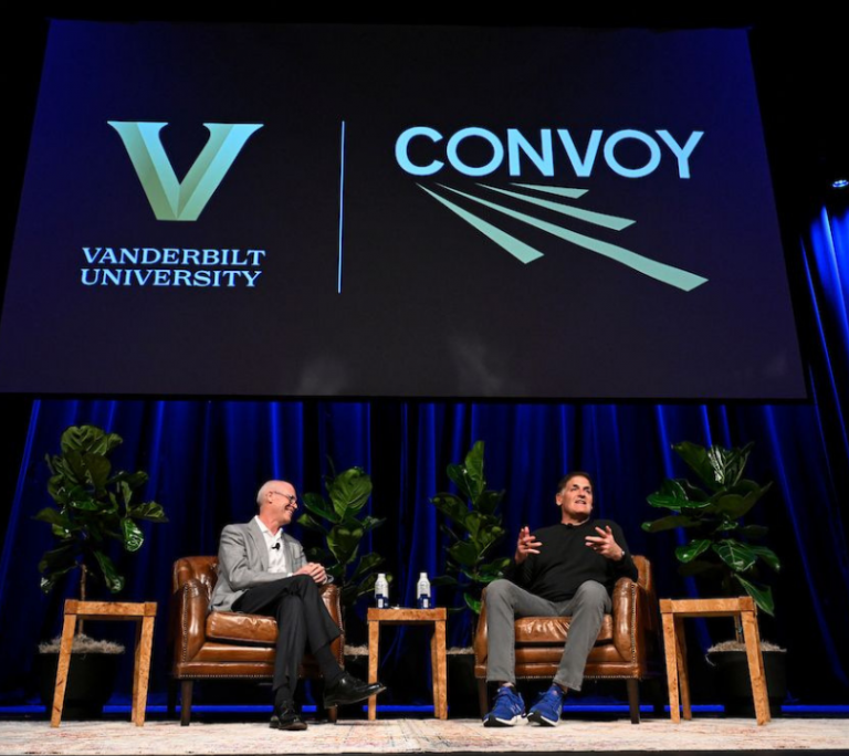 Two individuals seated in chairs on a stage with the Convoy and Vanderbilt logos on the screen behind them