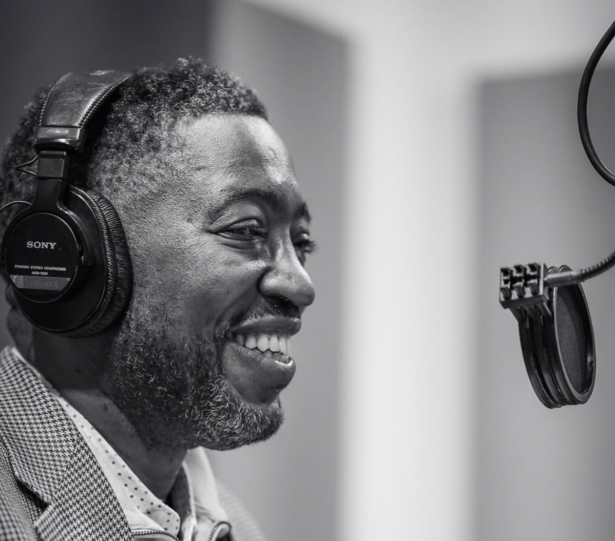 Major Jackson is seen in black and white smiling while talking into a podcast microphone.
