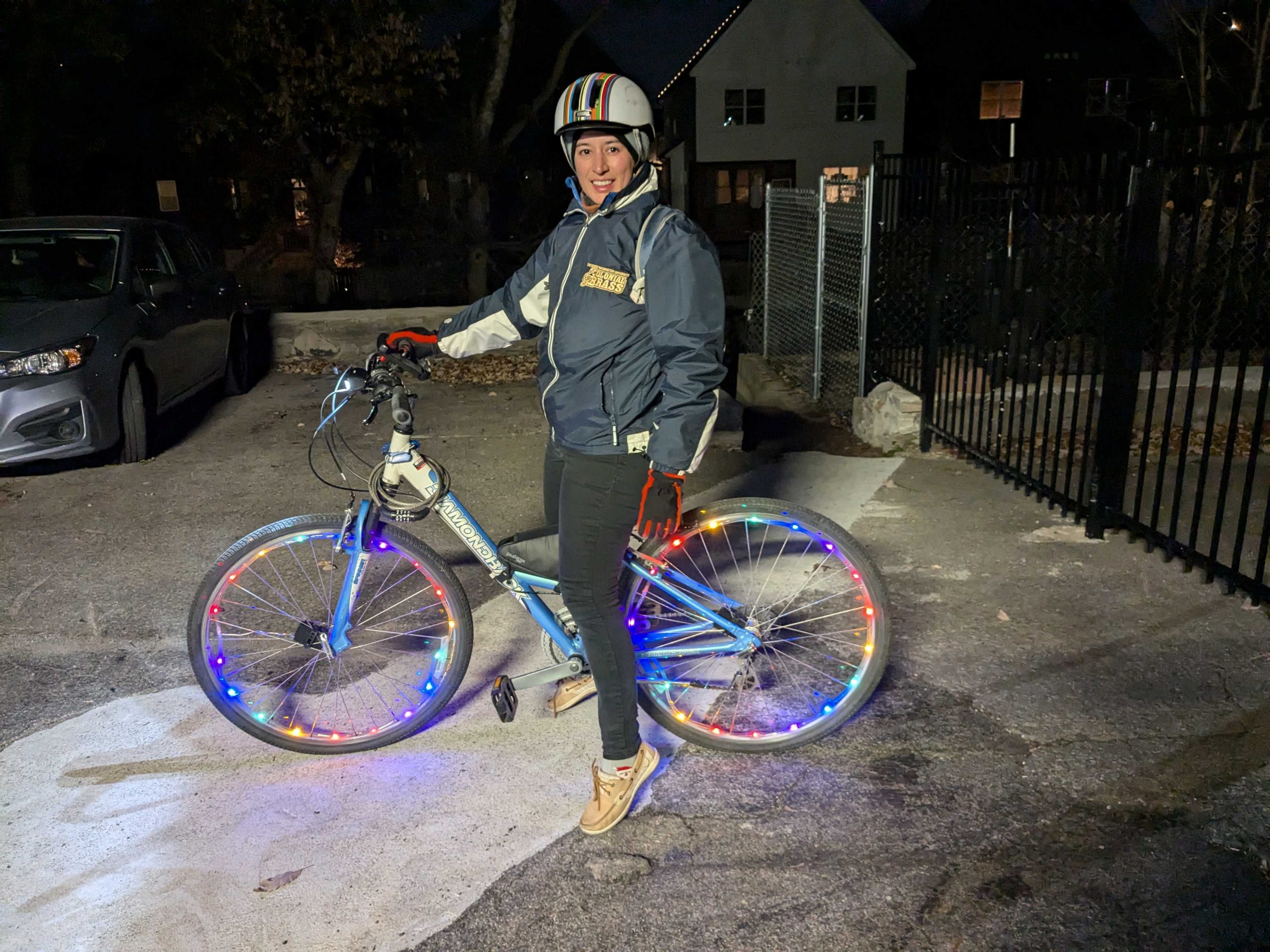 Woman riding bicycle with a helmet on and lit up wheels. 