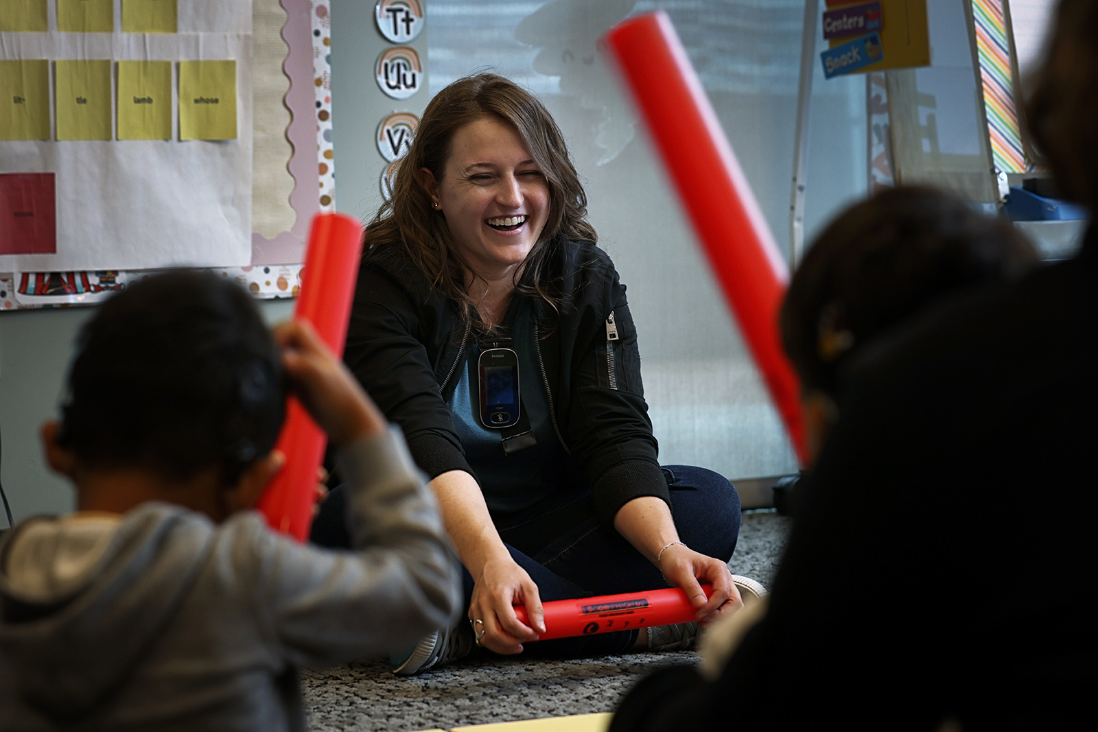 A young woman uses colorful plastic "boom whackers" to help preschoolers with hearing loss experience music.