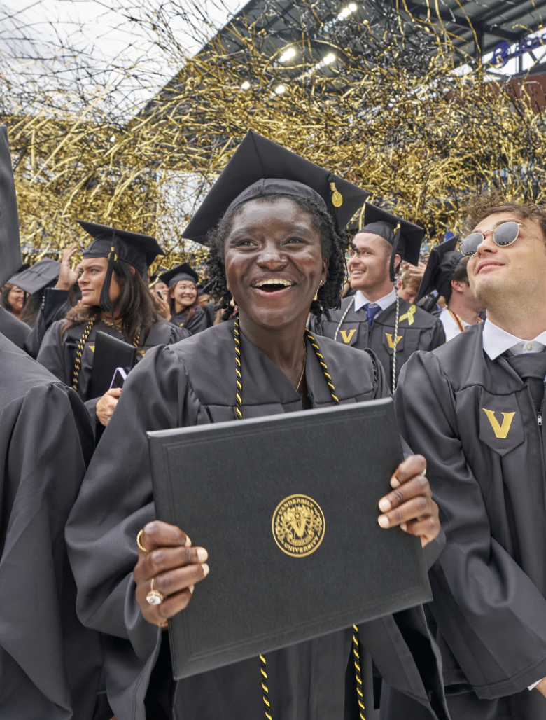 Students hold their diplomas and smile while confetti releases overhead at 2024 Commencement.